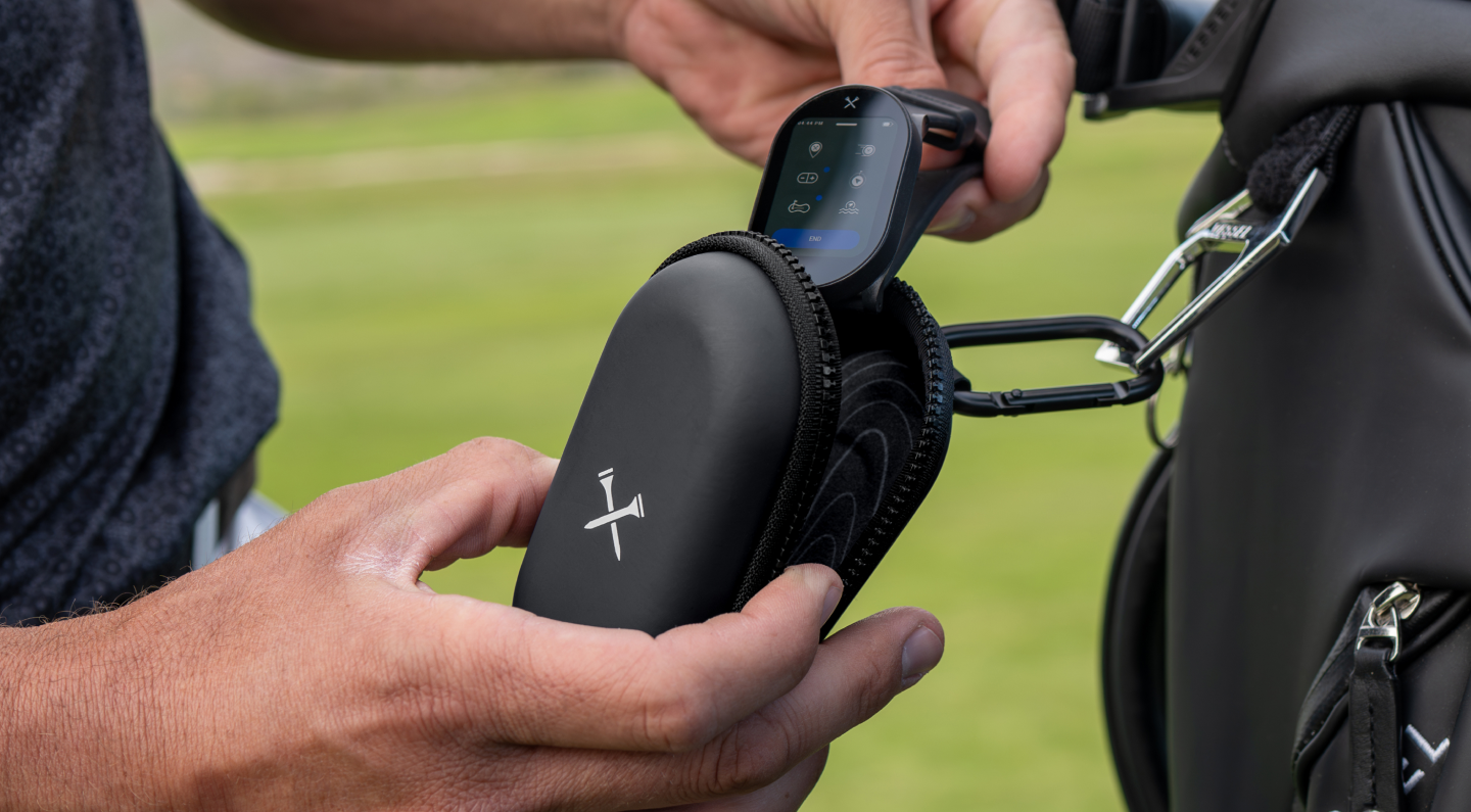 Person placing a handheld electronic device into a black zippered case attached to a golf bag.
